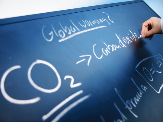 Eine Hand schreibt an einer Tafel mit Kreide die Worte "Global warming" und "CO2-Carbon Dioxide"